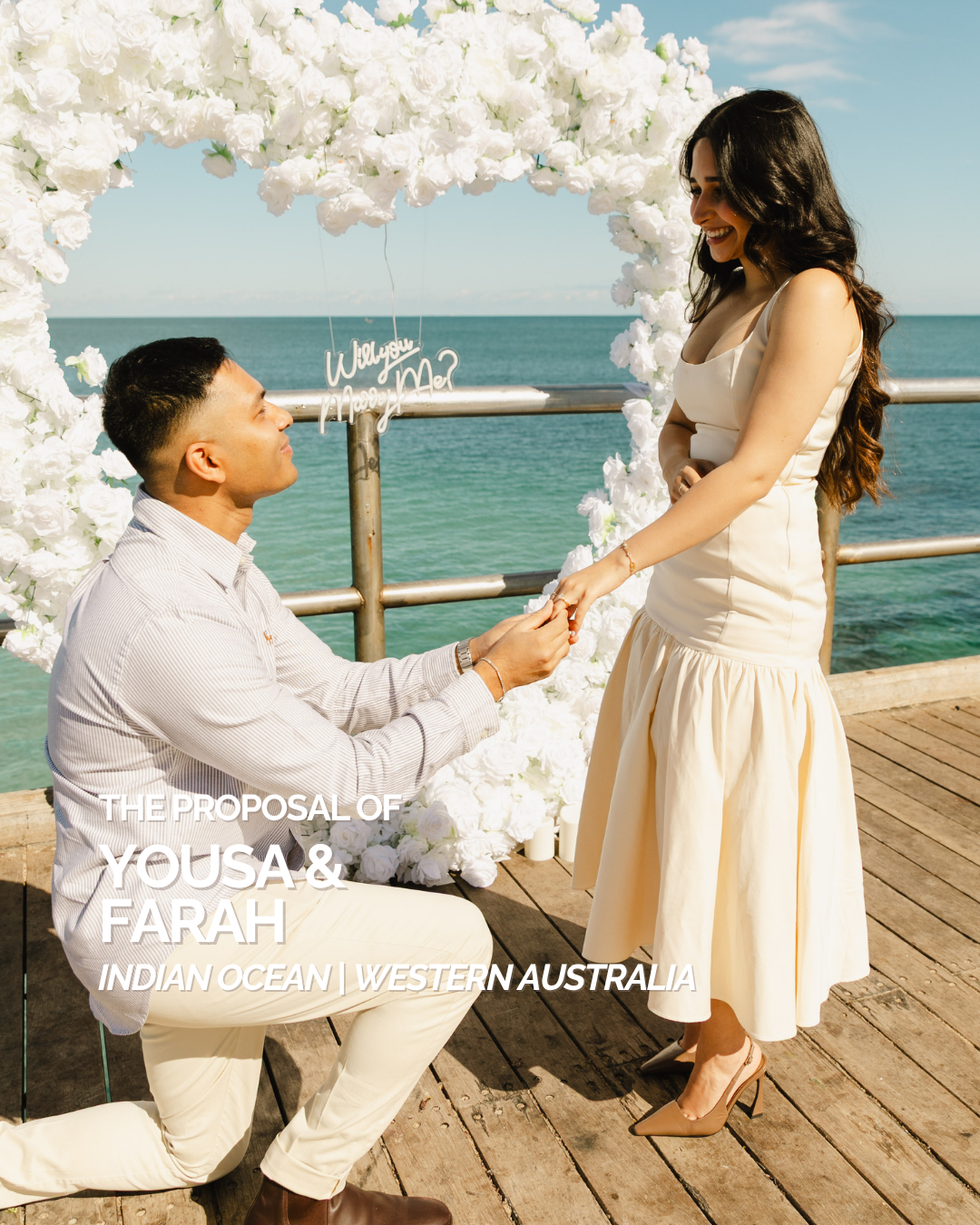 Man proposing to a woman with a white floral arch on a wooden deck by the ocean in Perth